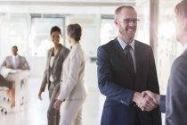 Men shaking hands, colleagues in background — Stock Photo