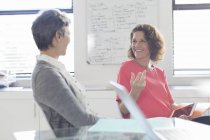 Two smiling women talking in office, whiteboard in background — Stock Photo