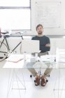 Porträt eines Mannes, der mit verschränkten Armen hinter einem gläsernen Schreibtisch im modernen Büro sitzt, Fahrrad und Whiteboard im Hintergrund — Stockfoto
