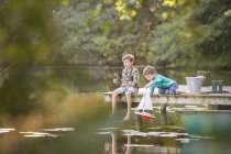 Хлопчики рибалять і грають з іграшковим вітрильником на озері — стокове фото