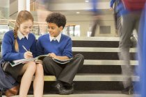 Grundschulkinder in Schuluniformen sitzen auf Stufen und schreiben in Schulbücher — Stockfoto