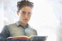 Retrato de estudante universitário com livro em pé ao lado da janela — Fotografia de Stock