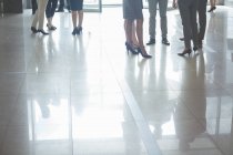 Baixa seção de empresários de pé no salão, com reflexões sobre piso de azulejos — Fotografia de Stock