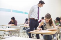 Чоловік вчитель контролює студентів, які пишуть екзамен GCSE в класі — стокове фото