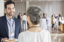 Бізнесмен розмовляє з бізнес-леді під час прийому в конференц-залі, тримає тарілку і шампанську флейту — стокове фото