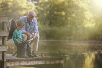 Abuelo y nieto leyendo en el lago - foto de stock