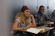 Studenti maschi e femmine sorridenti seduti alle scrivanie durante la lezione — Foto stock