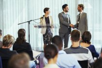 Businessmen shaking hands during presentation in conference room, businesswoman smiling — Stock Photo