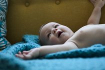 Портрет улыбающегося ребенка, лежащего на голубой ткани с вытянутыми руками — стоковое фото