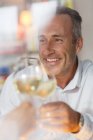 Lächelnder älterer Mann prostet mit Weißwein zu — Stockfoto