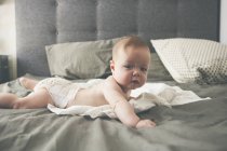 Ritratto del piccolo bambino sdraiato sul davanti sul letto con la testa sollevata — Foto stock