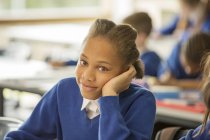 Portrait of smiling elementary school girl sitting bored in classroom — Stock Photo