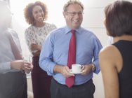Uomo d'affari che parla con i colleghi in carica e tiene in mano una tazza di caffè — Foto stock