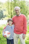 Дідусь і онук посміхаються на відкритому повітрі з футбольним м'ячем — стокове фото