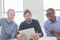 Трое улыбающихся мужчин, работающих с цифровыми планшетами в офисе — стоковое фото