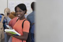 Retrato de estudiante universitario sonriente de pie en el pasillo, personas en segundo plano mirando los resultados del examen - foto de stock