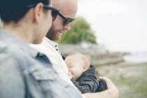 Батьки в сонцезахисних окулярах тримають маленьку дитину на відкритому повітрі — стокове фото