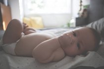 Porträt eines kleinen Babys, das Daumen lutscht, auf fleckigem Tuch liegend — Stockfoto