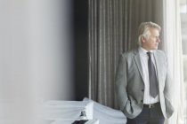 Porträt eines Geschäftsmannes mit Händen in Taschen, der im Konferenzraum steht und aus dem Fenster schaut — Stockfoto