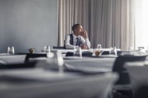 Портрет молодої людини, що сидить за столом у порожній конференц-залі, дивлячись крізь вікно — стокове фото