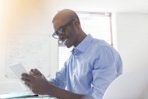 Jovem empresário sorrindo usando óculos e camisa azul usando tablet digital no escritório — Fotografia de Stock