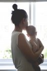 View of mother holding baby and looking through window — Stock Photo