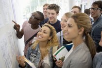Group of smiling students holding books and looking at information board — Stock Photo