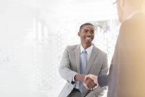 Hombres de negocios sonrientes estrechando las manos en la oficina - foto de stock