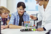 Teacher and students during chemistry lesson, wearing protective eyewear and looking at test tubes — Stock Photo