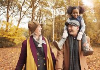 Laughing senior couple carrying daughter on shoulders in autumn woods — Stock Photo