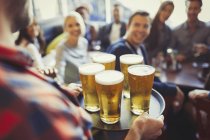 Barista che serve vassoio di birre agli amici nel bar — Foto stock