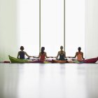 Donne su cuscini che si tengono per mano alla finestra in studio di palestra di yoga restaurativo — Foto stock