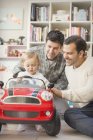 Чоловіки гей-батьки штовхають сина в іграшковий автомобіль — стокове фото