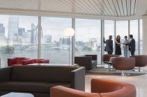 Geschäftsleute treffen sich an Fenstern in urbaner Hochhaus-Lounge — Stockfoto