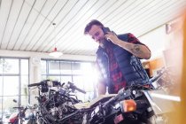 Motorcycle mechanic talking on cell phone in workshop — Stock Photo