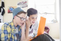Dos chicos adolescentes compartiendo portátil y auriculares en la habitación - foto de stock