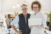Portrait of man and woman with laptop, smiling in office — Stock Photo