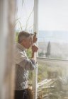 Senior man drinking coffee at sunny beach house window — Stock Photo