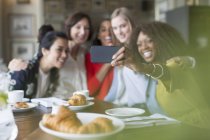 Sonriendo a las mujeres amigas tomando selfie con cámara de teléfono en el restaurante - foto de stock
