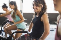 Smiling young woman riding elliptical bike in exercise class — Stock Photo