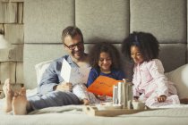 Hijas multiétnicas dando tarjetas al padre en la cama en el Día del Padre - foto de stock