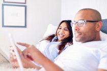 Smiling couple using digital tablet on bed — Stock Photo
