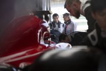 Manager und Formel-1-Rennfahrer im Gespräch in Reparaturwerkstatt — Stockfoto