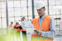 Инженер-мужчина рассматривает чертежи в буфере обмена на строительной площадке — стоковое фото