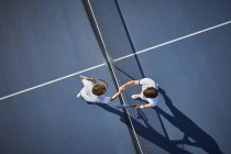 Вид сверху на молодых теннисистов, пожимающих руку в сетке на солнечном синем теннисном корте — стоковое фото