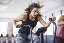 Determined young woman riding elliptical bike in gym — Stock Photo