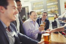 Hombres sonrientes amigos bebiendo cerveza en el bar - foto de stock