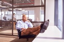 Pensive бізнесмен сидить з ногами вгору, дивлячись через сонячне вікно в офісі — стокове фото
