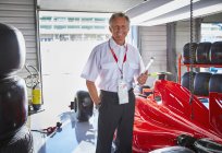 Portrait confident formula one manager next to race car in repair garage — Stock Photo