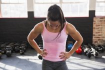 Tired, muscular young woman resting with hands on hips in gym — Stock Photo
